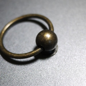 May include: A gold-toned metal ring with a round knob. The ring is smooth and has a polished finish.