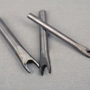 Puede incluir: Tres punzones de metal plateado con un extremo bifurcado. Los punzones se utilizan para la elaboración de cuero.
