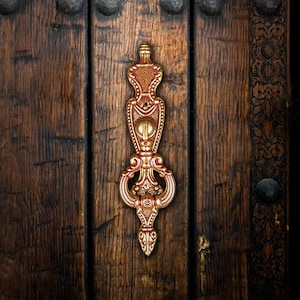 May include: An ornate door knocker with a gold and red design, mounted on a wooden door.