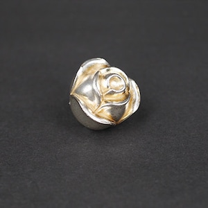 May include: A silver ring shaped like a rose with a gold centre.