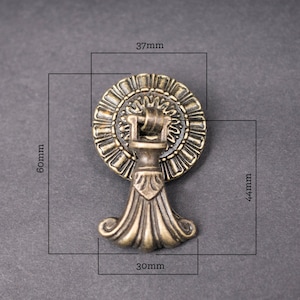 May include: Antique brass cabinet knob with a decorative floral design. The knob measures 37mm in diameter, 44mm in height, and 30mm in width.
