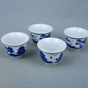 May include: Four white ceramic teacups with blue and white floral designs. The cups are arranged in a square shape on a grey surface.