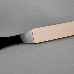 Puede incluir: Una correa de cuero con mango negro, utilizada para afilar navajas de afeitar.