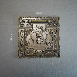 May include: A decorative brass latch with an ornate design, measuring 8.5 cm by 8.5 cm.