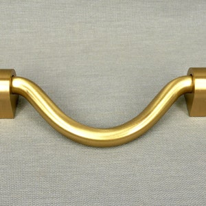 May include: A gold-toned, curved cabinet pull with a smooth, rounded finish. The pull has a simple, modern design and is ideal for adding a touch of elegance to any cabinet.
