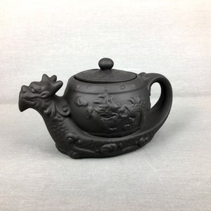 Peut inclure: Théière en céramique noire avec un motif de dragon. La théière a un couvercle et un bec verseur. Le dragon est en relief sur la théière.