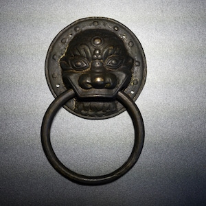 以下が含まれることがあります： ライオンの頭のデザインが施された黒い金属製のドアノッカー。ノッカーにはリングハンドルが付いています。