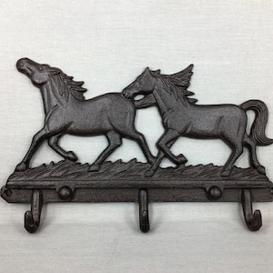May include: A cast iron key holder with a design of two horses running. The key holder has three hooks.