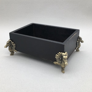 May include: A black wooden box with decorative gold horse head feet. The box is empty and ready to be filled.