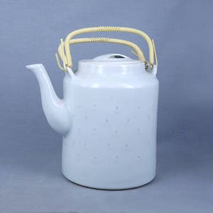 Può includere: Una teiera in ceramica bianca con un design maculato e un manico in bambù. La teiera ha un corpo arrotondato e un beccuccio laterale.