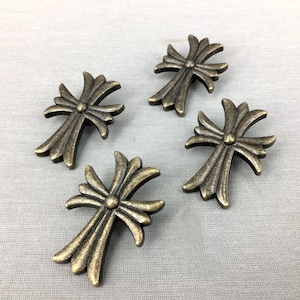 May include: Four antique gold-toned metal cross-shaped drawer pulls with a decorative design.