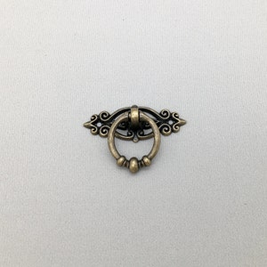 May include: A decorative antique gold-toned metal ring pull with a scrolled design.