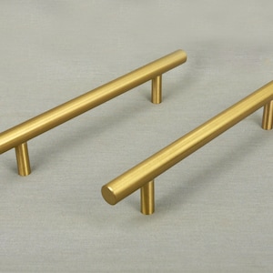 May include: Two gold-toned cabinet pulls with a straight bar design and a T-shaped handle.