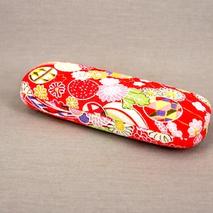 Könnte beinhalten: Ein rotes und weißes Brillenetui mit floralem Muster. Das Etui ist aus Stoff und hat eine abgerundete Form.