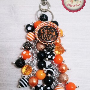 May include: A Halloween-themed keychain with a black and orange bottle cap charm that says "Witch Please". The keychain also features a variety of black, orange, and white beads.
