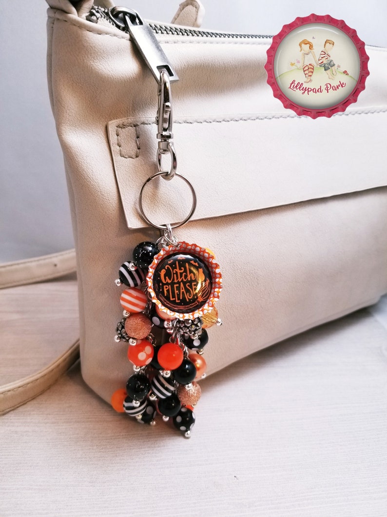May include: A black and orange Halloween-themed keychain with a charm that says "Witch Please". The keychain is attached to a silver key ring and has a variety of beads, including black and white striped beads, orange beads, and black beads with white polka dots.