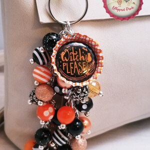 May include: A black and orange Halloween-themed keychain with a bottle cap charm that says "Witch Please". The keychain features a variety of black, white, orange, and gold beads.