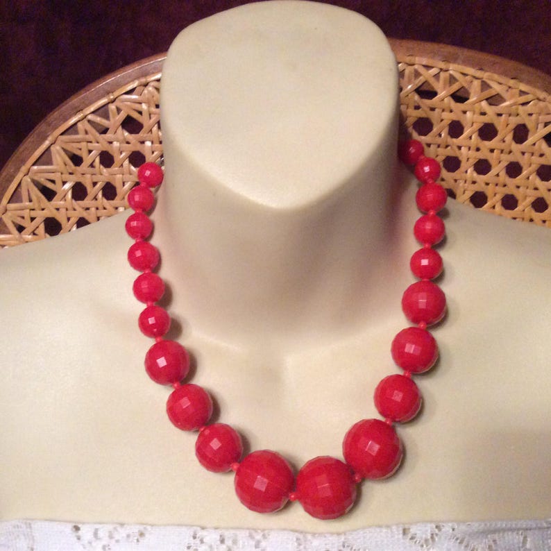 May include: A red beaded necklace with large, faceted beads. The necklace is on a white mannequin bust.