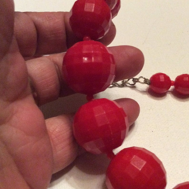 May include: A red beaded necklace with large, faceted beads. The beads are connected by a silver chain.