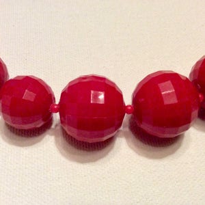 May include: A close-up of a red beaded necklace. The beads are large and have a faceted, geometric design.