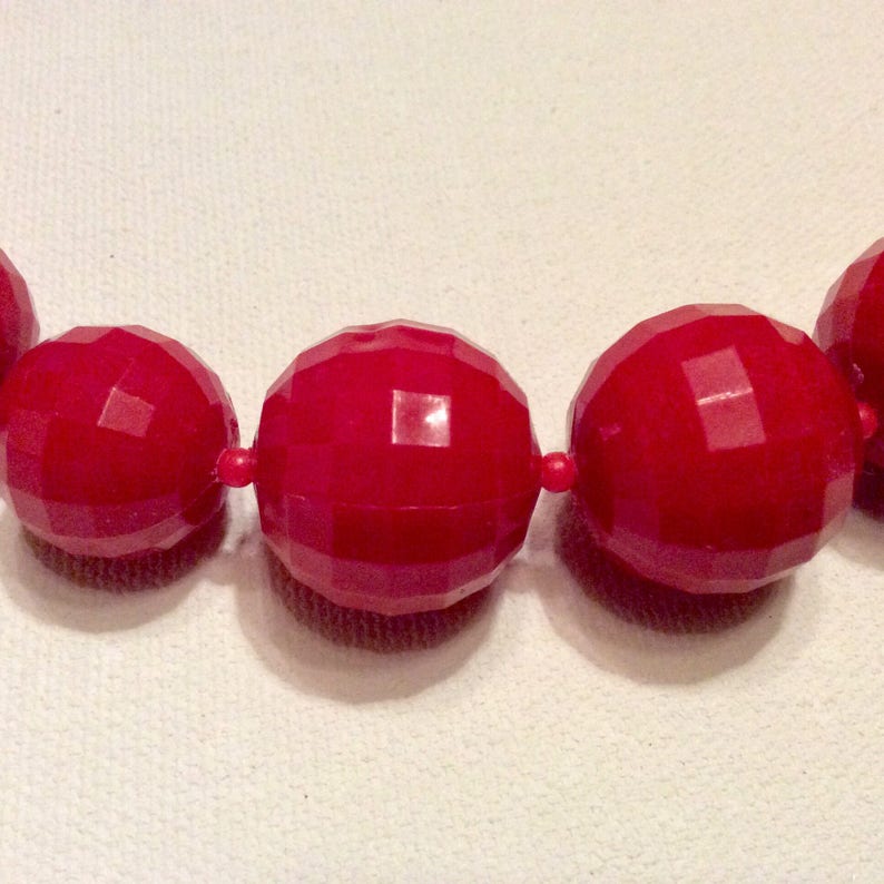 May include: A close-up of a red beaded necklace. The beads are large and have a faceted, geometric design.