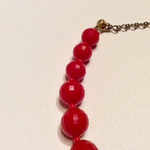 May include: A red beaded necklace with a gold clasp. The beads are faceted and have a glossy finish.