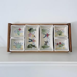 May include: A wooden serving tray with six ceramic dishes. The dishes feature hand-painted desert-themed illustrations of cacti, flowers, and cartoon figures. The tray is made of dark wood.