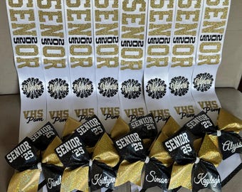 Puede incluir: Ocho fajas blancas con texto negro que dice "Senior 2025" y un nombre en cada faja. Cada faja tiene un lazo de animadora negro y dorado con el nombre escrito en el lazo. Las fajas son para un equipo de animadora de la escuela secundaria.