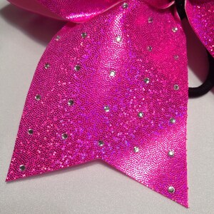 May include: A bright pink cheer bow with silver glitter and rhinestones. The bow has a black elastic band for attaching to hair.
