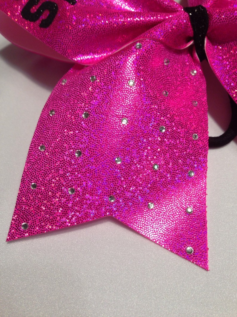 May include: A bright pink cheer bow with silver glitter and rhinestones. The bow has a black elastic band for attaching to hair.