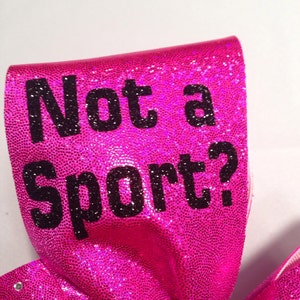 May include: A pink cheer bow with black glitter and the text "Not a Sport?" printed on it.