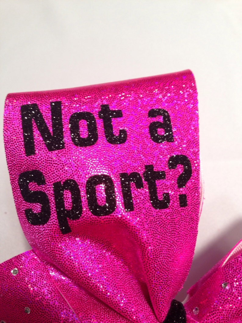 May include: A pink cheer bow with black glitter and the text "Not a Sport?" printed on it.