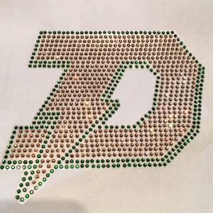 May include: A green and gold letter D made of rhinestones. The letter is outlined in green rhinestones and filled in with gold rhinestones.