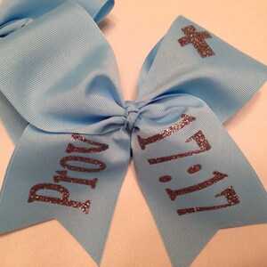 May include: A light blue cheer bow with silver glitter lettering that says "Pray" and "11:11" with a silver glitter cross on one side.