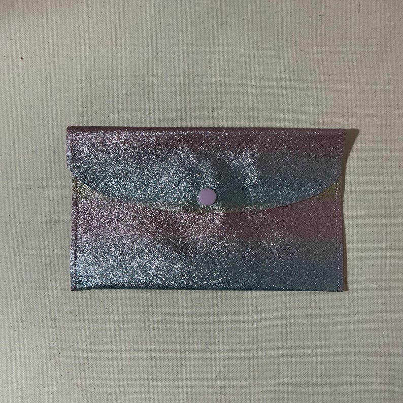 May include: A silver and pink glitter clutch with a pink button closure.