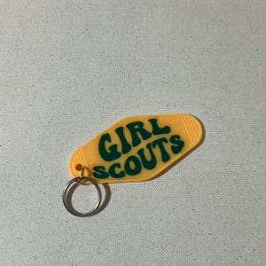 May include: A yellow plastic keychain shaped like a motel key with the text "GIRL SCOUTS" in green letters.