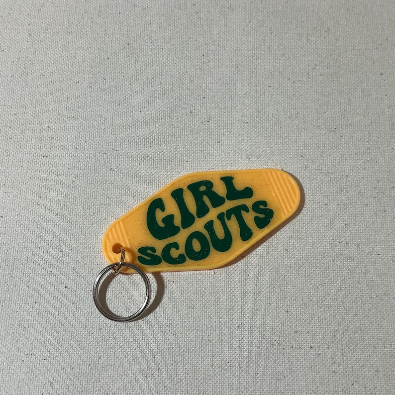 May include: A yellow plastic keychain shaped like a motel key with the text "GIRL SCOUTS" in green letters.