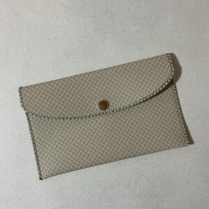 May include: A beige leather clutch with a geometric pattern and a gold button closure.