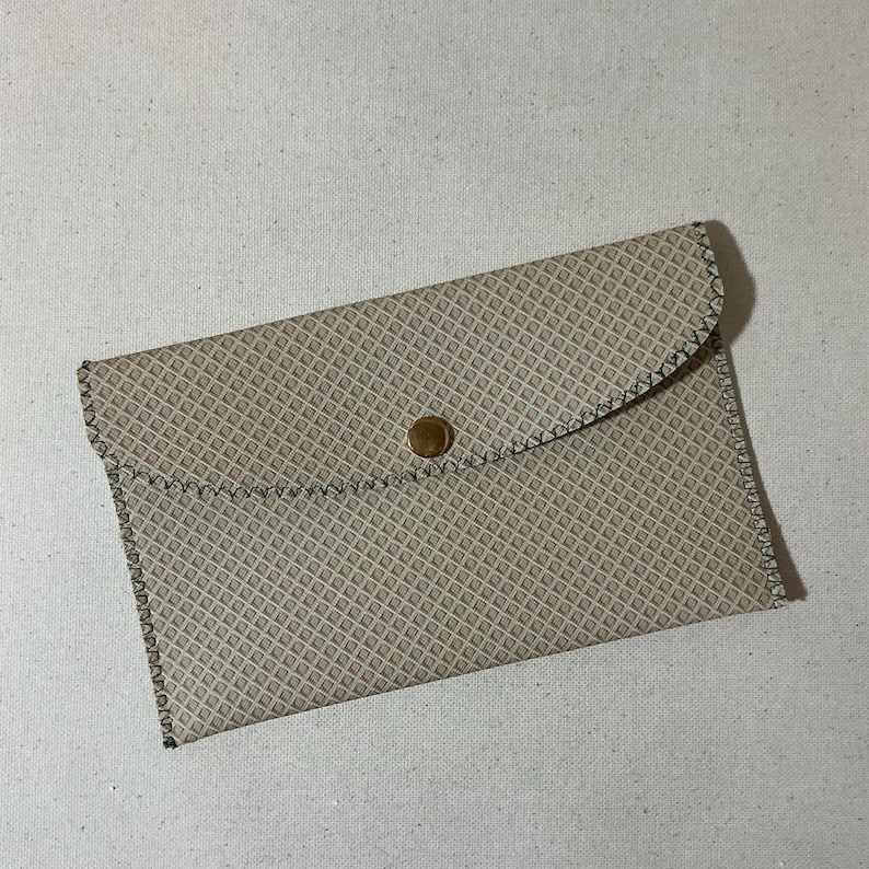 May include: A beige leather clutch with a geometric pattern and a gold button closure.