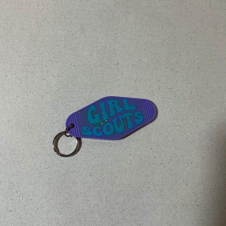 May include: Purple motel key chain with a blue glitter 'GIRL SCOUTS' design.