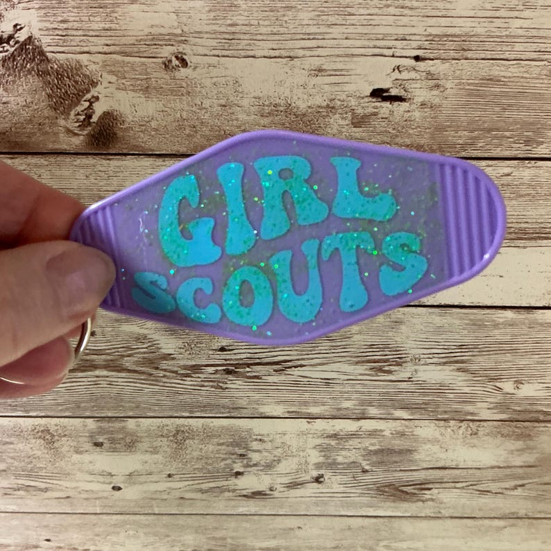 May include: Purple motel key chain with the words "GIRL SCOUTS" in turquoise glitter lettering.