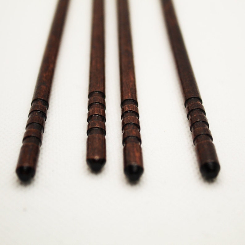 May include: Four brown wooden chopsticks with a dark brown finish and a ridged design.