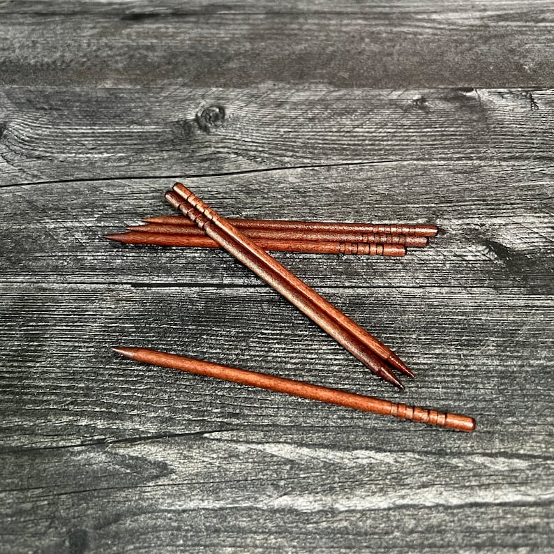 May include: A set of six brown wooden chopsticks on a gray wooden surface.