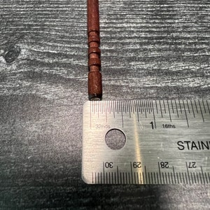 May include: A close-up of a wooden dowel rod with a ruler measuring 1 inch in length. The ruler is marked in 16ths and 32nds of an inch.