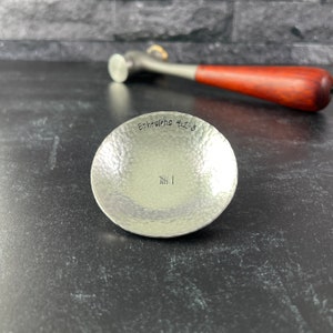 May include: A small, silver, hammered metal dish with the words "Ephesians 4:2-3" and a series of hash marks engraved on the inside.