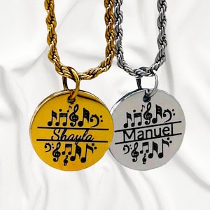 May include: Two gold and silver necklaces with round pendants featuring musical notes and the names "Shayla" and "Manuel".