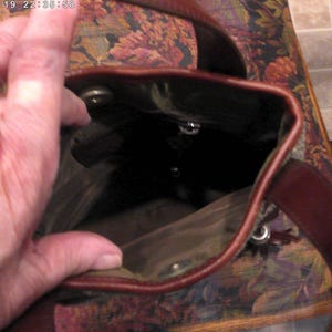 May include: A brown leather bucket bag with a dark interior lining, featuring a top opening with a magnetic snap closure and a sturdy leather shoulder strap. The bag has a deep, open main compartment and visible metal hardware accents.