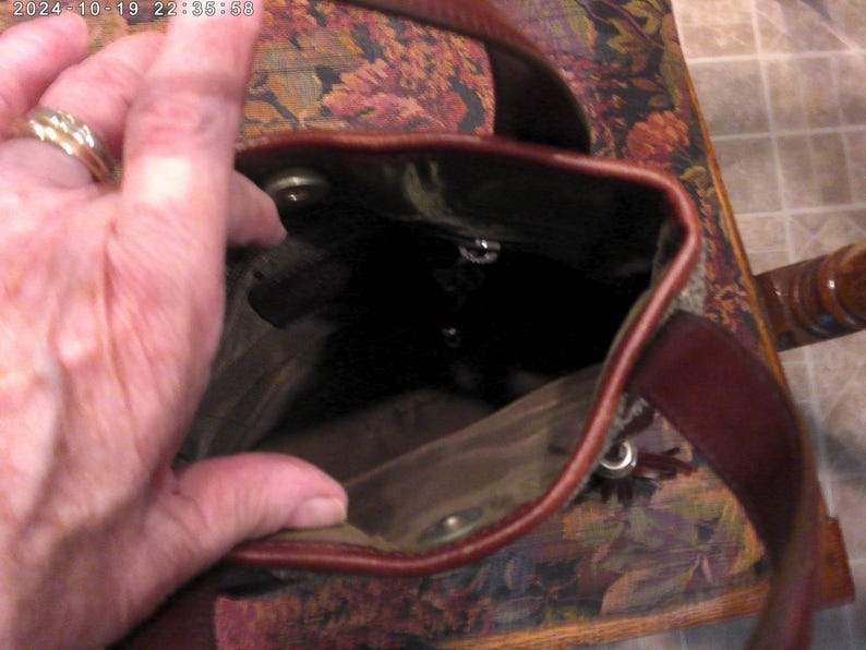 May include: A brown leather bucket bag with a dark interior lining, featuring a top opening with a magnetic snap closure and a sturdy leather shoulder strap. The bag has a deep, open main compartment and visible metal hardware accents.