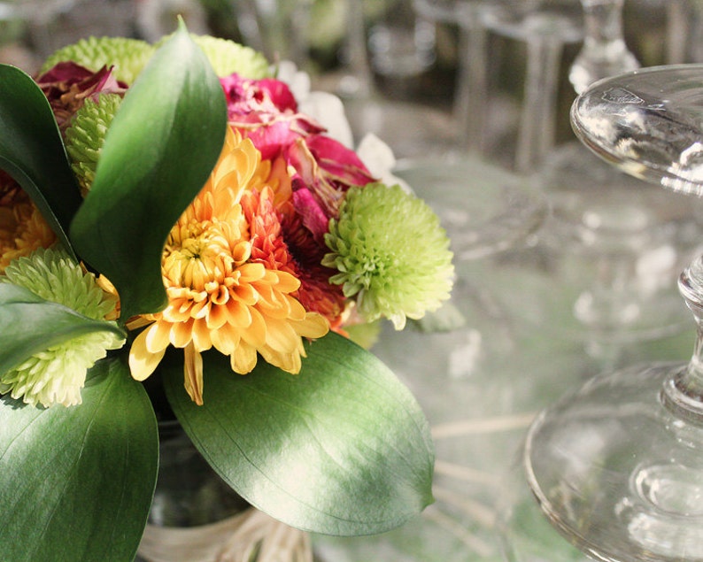 May include: A bouquet of flowers with yellow, orange, pink, and green blooms. The flowers are arranged in a clear glass vase with green leaves.