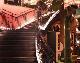 May include: A black metal staircase with a white string of lights winding up the steps. A large green palm tree with a sign that reads "Watch Out Falling Coconuts" is in the background.